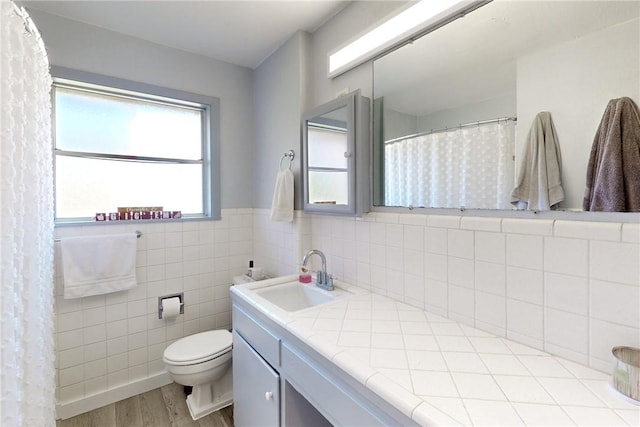 bathroom with toilet, wood-type flooring, vanity, and tile walls