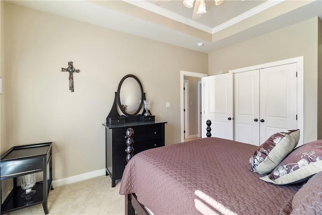 bedroom with light colored carpet, baseboards, ornamental molding, a closet, and a tray ceiling