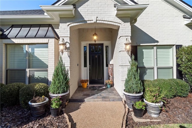 doorway to property with a standing seam roof, metal roof, and brick siding