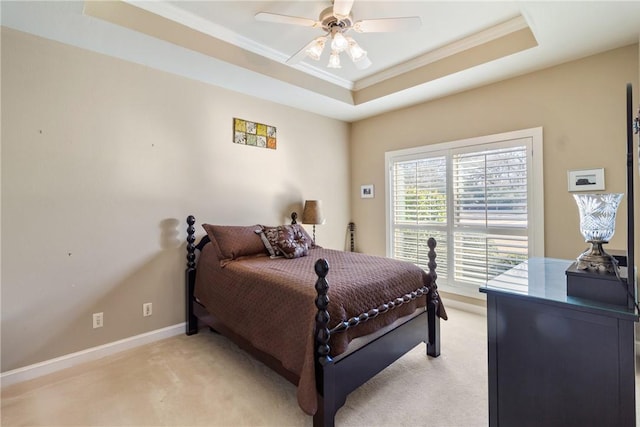 bedroom featuring light carpet, baseboards, a ceiling fan, ornamental molding, and a tray ceiling