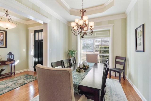 dining space with a chandelier, baseboards, light wood finished floors, ornamental molding, and a tray ceiling