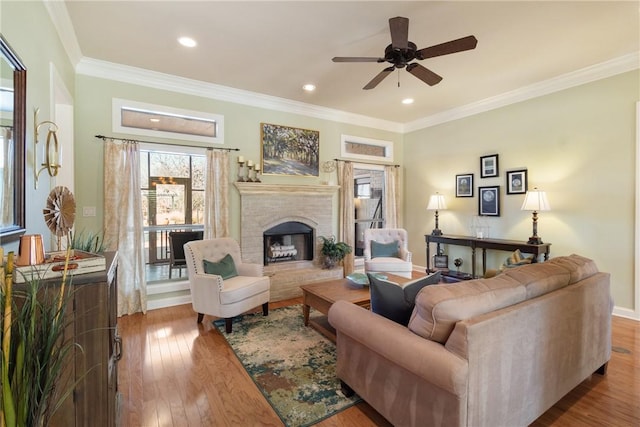 living area featuring crown molding, hardwood / wood-style floors, a brick fireplace, ceiling fan, and baseboards