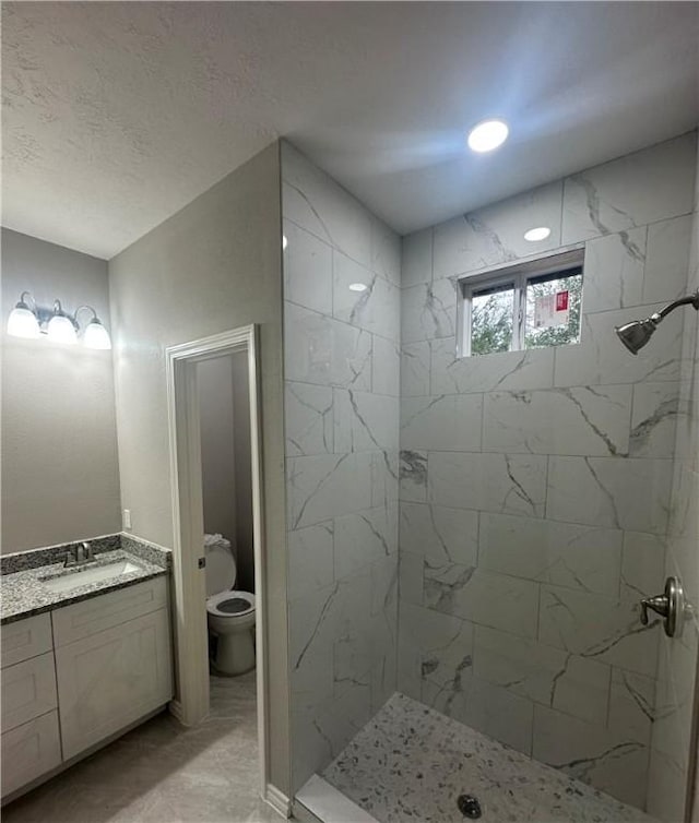 bathroom featuring a textured ceiling, toilet, vanity, and tiled shower