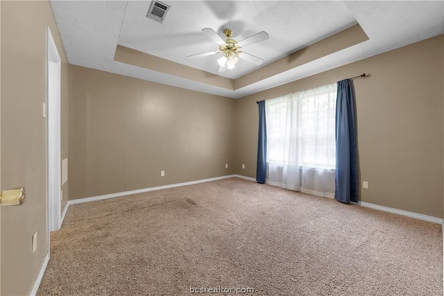 empty room with carpet flooring, ceiling fan, and a raised ceiling