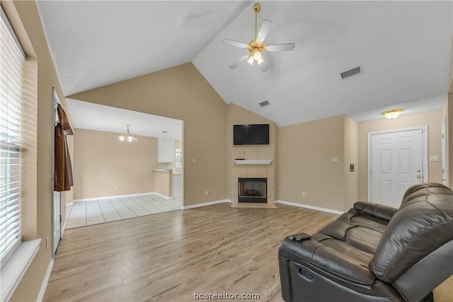 living room with ceiling fan with notable chandelier, light wood-type flooring, high vaulted ceiling, and a tiled fireplace