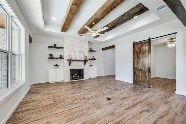 unfurnished living room with a barn door, a fireplace, visible vents, a ceiling fan, and light wood finished floors