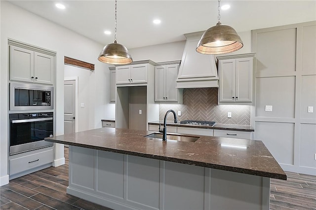 kitchen with sink, hanging light fixtures, dark stone countertops, custom range hood, and appliances with stainless steel finishes