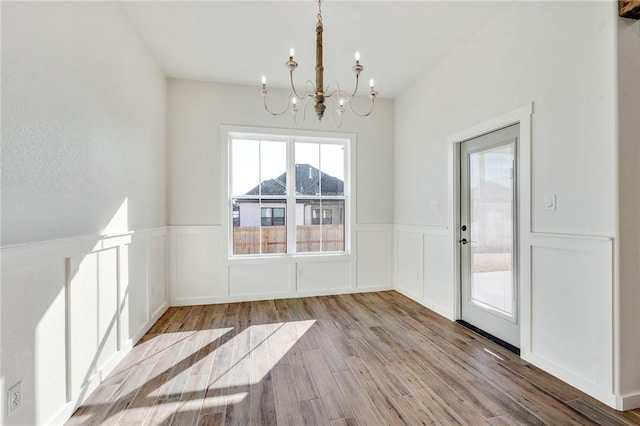 entryway with a wainscoted wall, a decorative wall, an inviting chandelier, and wood finished floors