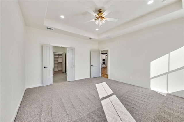 unfurnished bedroom featuring light carpet, visible vents, a tray ceiling, and baseboards