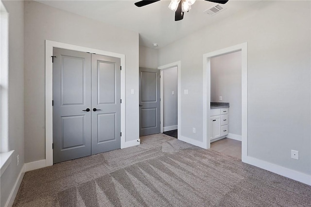 unfurnished bedroom featuring ceiling fan, a closet, ensuite bathroom, and light carpet