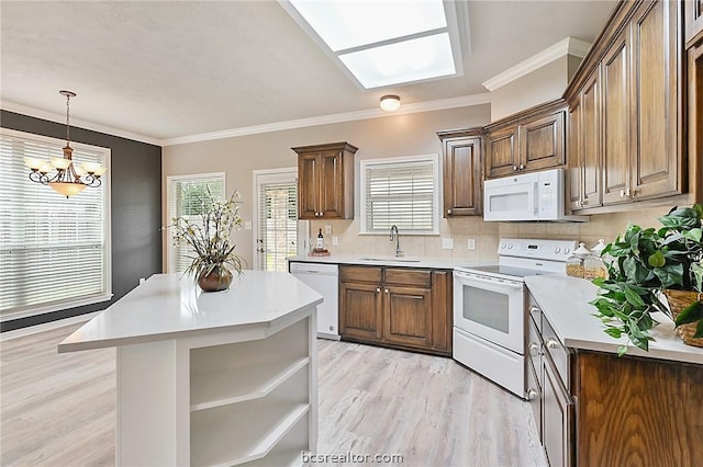 kitchen featuring a skylight, sink, an inviting chandelier, light hardwood / wood-style floors, and white appliances