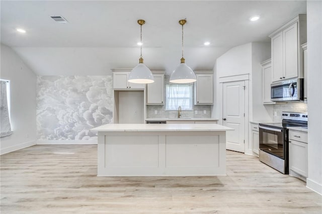 kitchen with a center island, light wood-style floors, appliances with stainless steel finishes, light countertops, and lofted ceiling