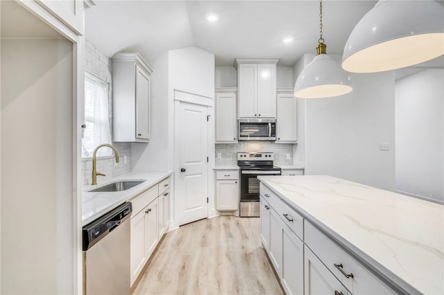 kitchen featuring a sink, backsplash, stainless steel appliances, light wood-style floors, and light stone countertops