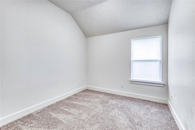 carpeted spare room featuring vaulted ceiling and baseboards