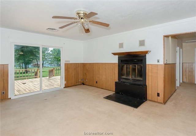 unfurnished living room featuring ceiling fan, wood walls, crown molding, and light carpet