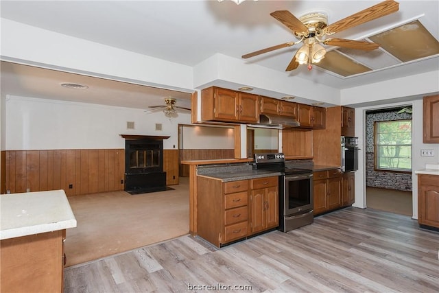 kitchen with appliances with stainless steel finishes, ceiling fan, light hardwood / wood-style flooring, a wood stove, and wood walls