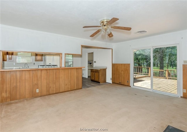 unfurnished living room with light carpet, ceiling fan, crown molding, and sink