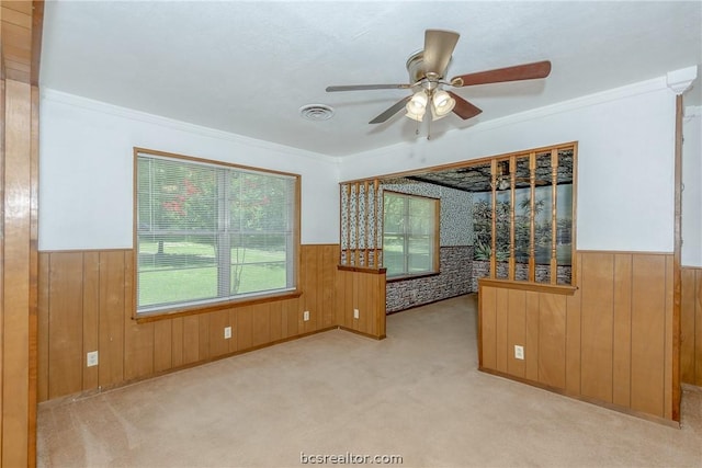 carpeted empty room featuring ceiling fan, wood walls, and ornamental molding