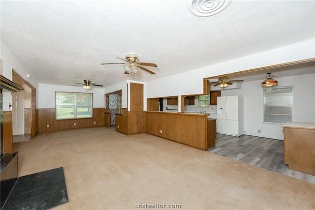 kitchen featuring kitchen peninsula, wood walls, carpet floors, and white refrigerator with ice dispenser