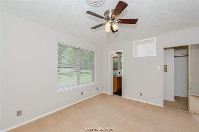 unfurnished bedroom with ceiling fan, light colored carpet, and ensuite bathroom