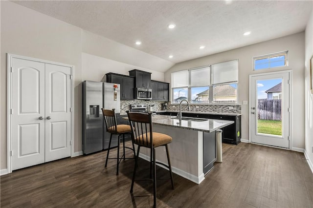 kitchen with a center island with sink, backsplash, appliances with stainless steel finishes, a sink, and light stone countertops