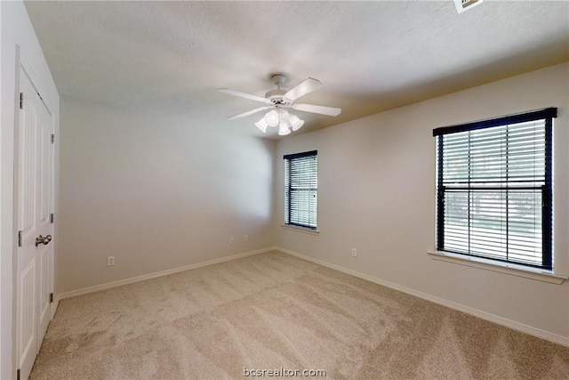 empty room with plenty of natural light, ceiling fan, light colored carpet, and a textured ceiling