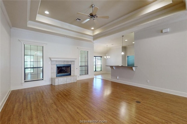 unfurnished living room with hardwood / wood-style floors, a tile fireplace, ceiling fan with notable chandelier, ornamental molding, and a tray ceiling