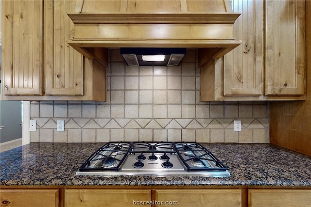 kitchen with decorative backsplash, premium range hood, stainless steel gas stovetop, and dark stone counters