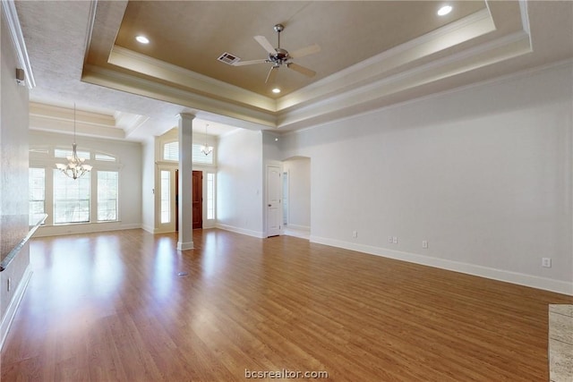 unfurnished living room with a tray ceiling, wood-type flooring, ceiling fan with notable chandelier, and ornamental molding