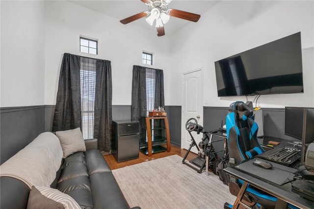 office space with a towering ceiling, ceiling fan, and light wood-type flooring