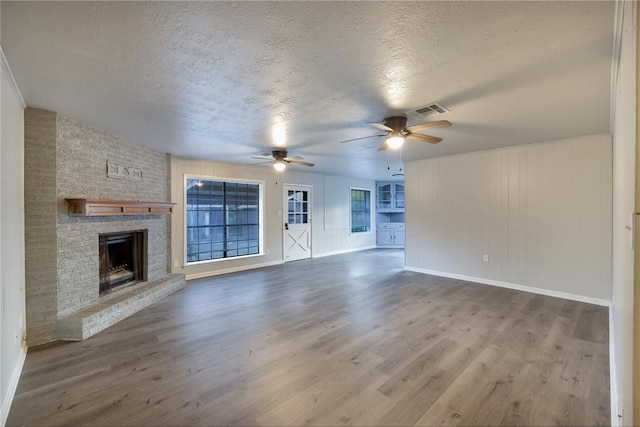 unfurnished living room featuring ceiling fan, a fireplace, wood-type flooring, and a textured ceiling