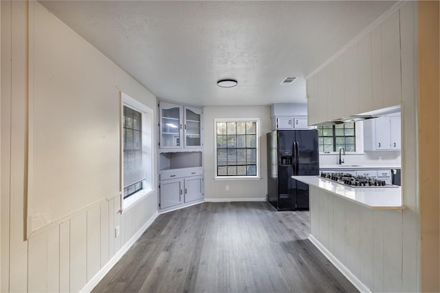 kitchen with stainless steel gas stovetop, dark wood-type flooring, black refrigerator with ice dispenser, a textured ceiling, and white cabinetry