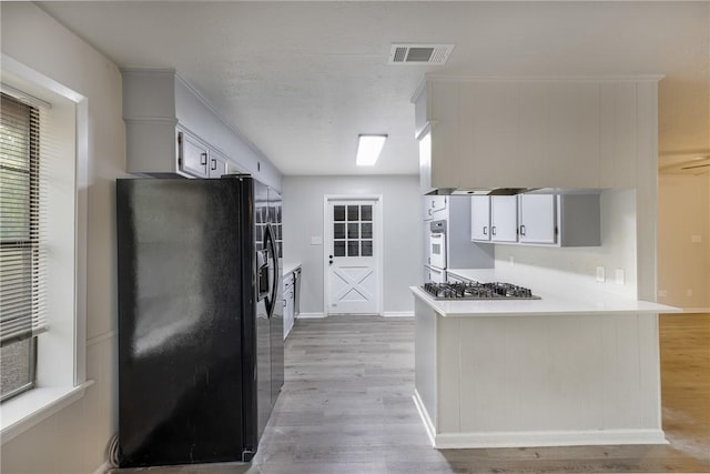 kitchen featuring white double oven, black refrigerator, light hardwood / wood-style floors, kitchen peninsula, and stainless steel gas cooktop