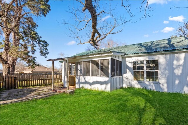 rear view of house featuring a yard, a sunroom, metal roof, and fence