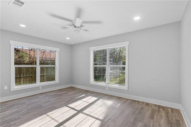 unfurnished room featuring a wealth of natural light, visible vents, a ceiling fan, wood finished floors, and baseboards
