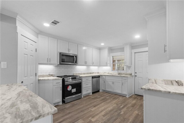 kitchen with ornamental molding, white cabinetry, appliances with stainless steel finishes, decorative backsplash, and dark wood-style flooring