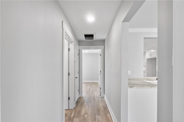 hall with light wood finished floors, visible vents, and baseboards