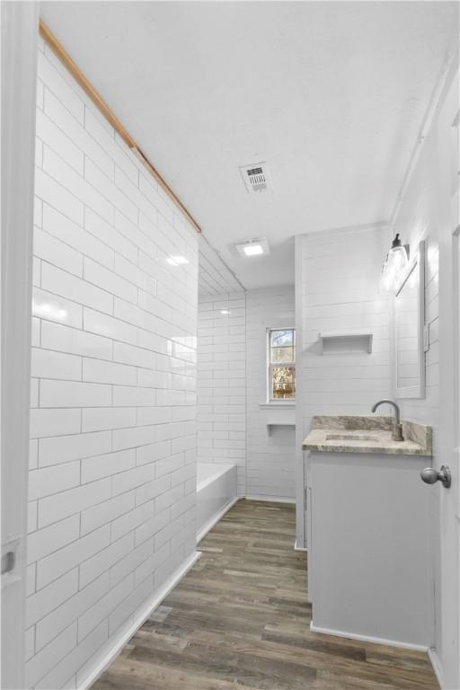 bathroom with vanity, wood finished floors, visible vents, and a tub to relax in