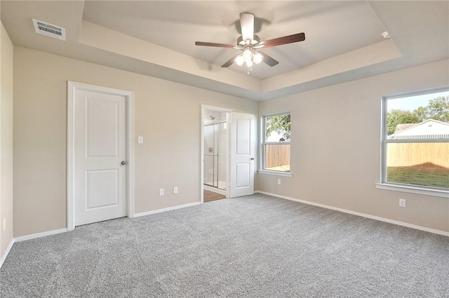 unfurnished bedroom with ceiling fan, a raised ceiling, carpet floors, and ensuite bath