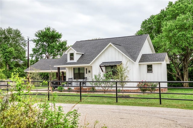 modern farmhouse with a porch, a fenced front yard, roof with shingles, and board and batten siding