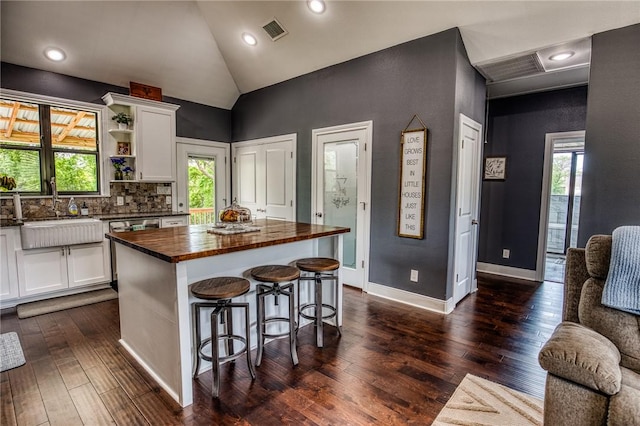 kitchen featuring visible vents, a center island, white cabinets, a sink, and wood counters