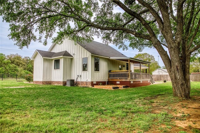 back of house featuring fence, central AC unit, board and batten siding, and a lawn