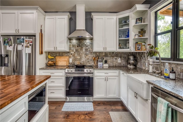 kitchen featuring wall chimney range hood, stainless steel appliances, white cabinetry, dark wood-type flooring, and butcher block counters