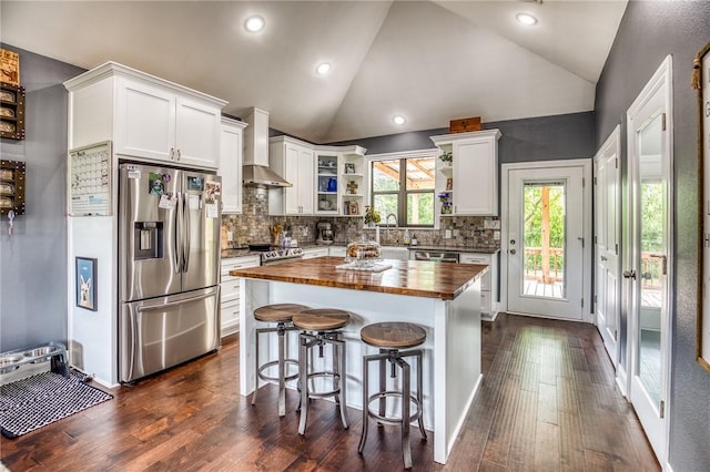 kitchen featuring wall chimney range hood, butcher block counters, lofted ceiling, stainless steel appliances, and white cabinetry