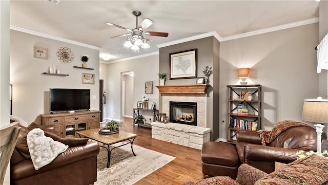 living room with a ceiling fan, a stone fireplace, ornamental molding, and wood finished floors
