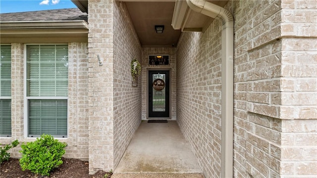 entrance to property featuring a shingled roof and brick siding