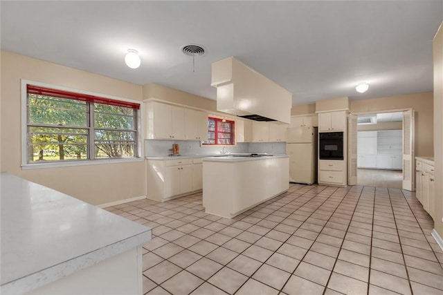 kitchen featuring white cabinets, black oven, white fridge, and custom range hood