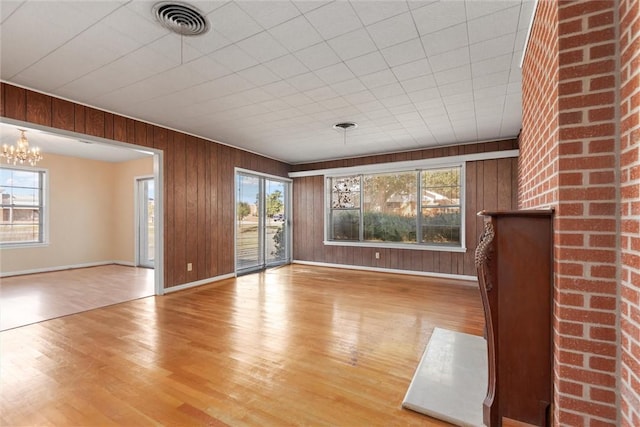 unfurnished living room featuring hardwood / wood-style floors, wooden walls, and a notable chandelier