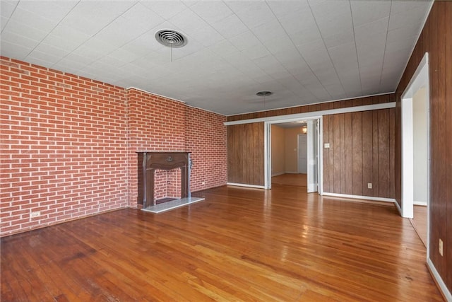 unfurnished living room featuring wood walls, brick wall, and hardwood / wood-style flooring