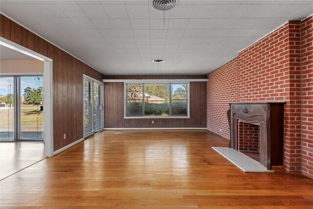 unfurnished living room with light wood-type flooring, a large fireplace, wooden walls, and brick wall